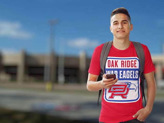 Person wearing a red 'Oak Ridge War Eagles' t-shirt with a backpack, holding a phone, against a blurred outdoor background.