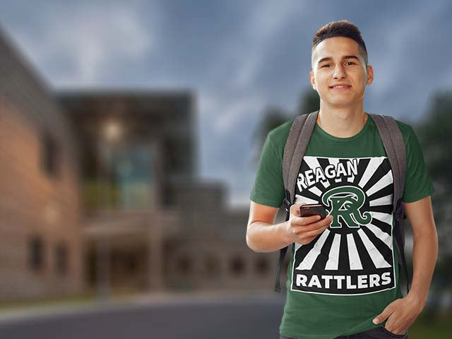 Person wearing a green t-shirt with 'Reagan Rattlers' design, holding a phone, with a blurred background.