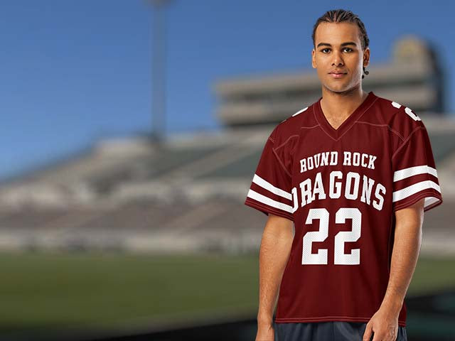 A man wearing a maroon and white football jersey with 'ROUND ROCK DRAGONS 22' printed on the front, standing against a blurred stadium background.