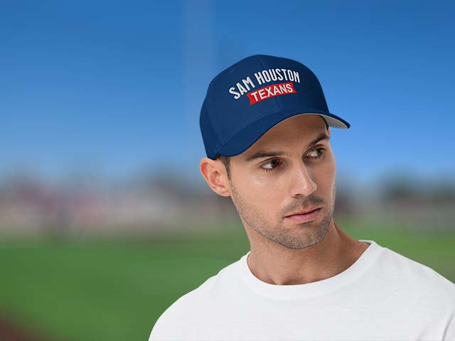 A man wearing a navy blue baseball cap with 'SAM HOUSTON TEXANS' embroidered on the front, set against a blurred outdoor background of blue sky and green field.