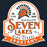 A distressed school spirit logo for Seven Lakes High School Spartans, featuring an orange and black Spartan helmet with a sunburst crest on a white shield-shaped background with orange and black text, set against a dark navy background. 