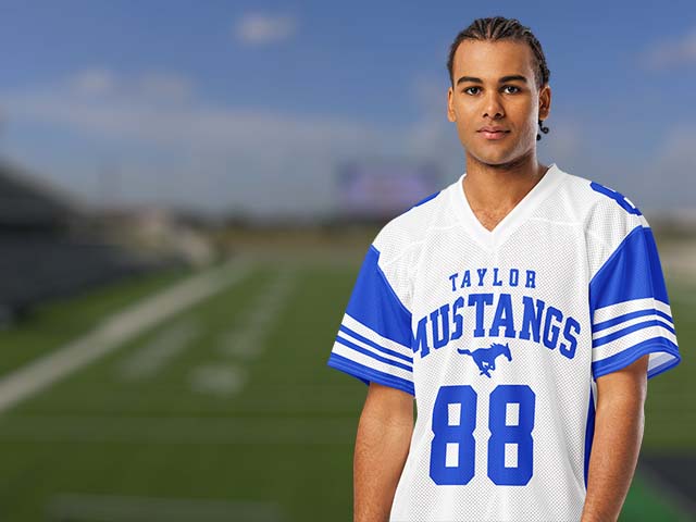 A man wearing a white and blue football jersey with 'Taylor Mustangs' and the number 88, standing on a blurred football field under a blue sky.